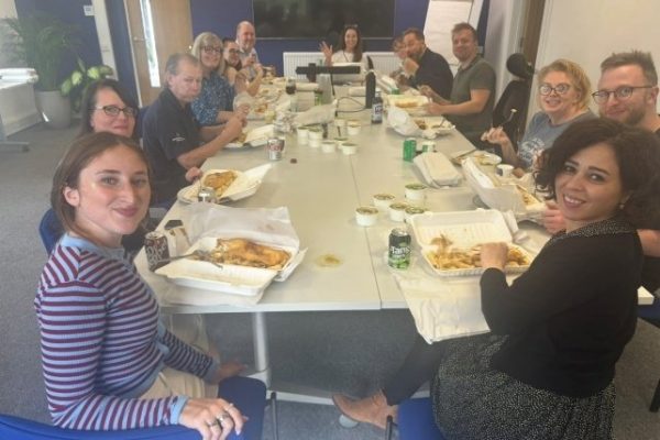 Colleagues seated along a long meeting table enjoying fish and chips at Head Office