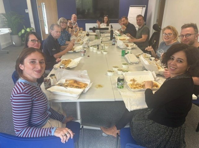 Colleagues seated along a long meeting table enjoying fish and chips at Head Office