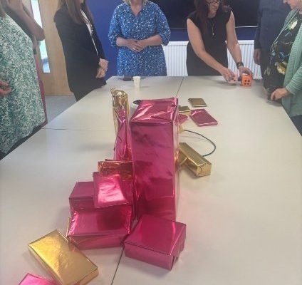 Colleagues gathered around a table stacked with pink and gold wrapped prizes for the Dice Game