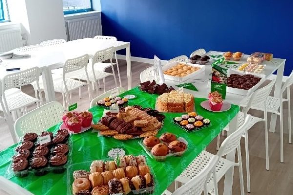 Tables covered in green Macmillan cloths and laid out with cakes, doughnuts and pastries for the coffee morning