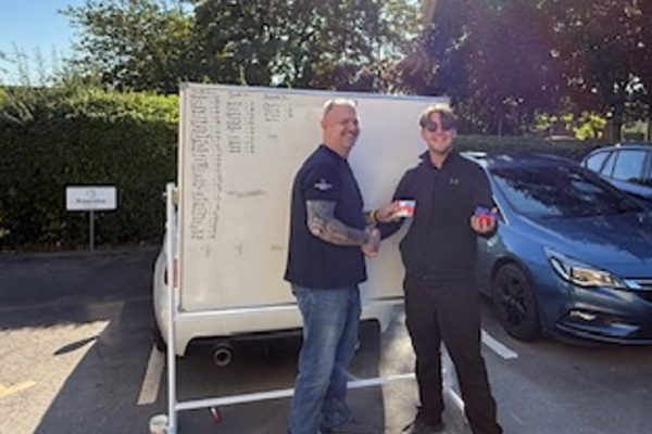 Two colleagues with a prize in front of the outdoor scoreboard after the Bean Bag Toss Challenge