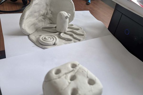 Roger's unpainted air-dry clay octopus in front of a curved shell, with his clay dice in the foreground