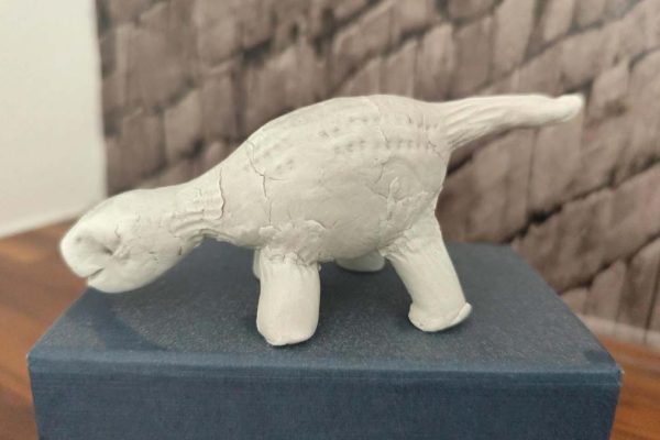 Konstantin's unpainted air-dry clay dinosaur with a long tail, standing on a blue box