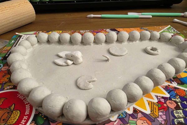 Amy's unpainted clay pond ring dish, edged with pebbles and holding lily pads, a small creature and a rubber ring