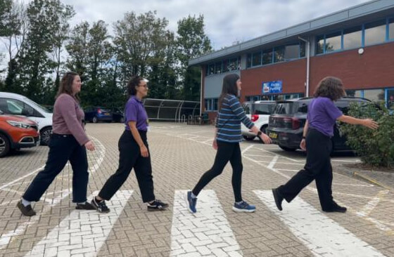 Four colleagues walking in single file across a zebra crossing in the car park, recreating the Beatles' Abbey Road album cover
