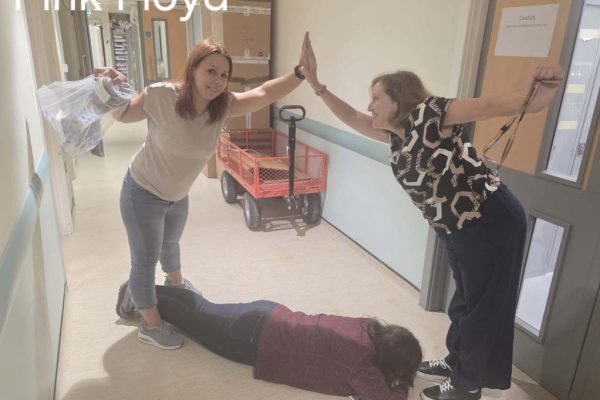 Labelled "Pink Floyd": two colleagues high-fiving in a corridor over a third lying face down on the floor, recreating an album cover